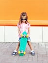 Fashion little girl child with skateboard wearing sunglasses and checkered shirt in city Royalty Free Stock Photo