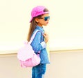 Fashion little girl child wearing sunglasses, baseball cap, backpack in profile on white Royalty Free Stock Photo