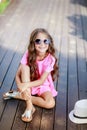 Fashion little girl model wearing a pink checkered shirt, hat and sunglasses in city Royalty Free Stock Photo