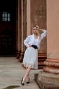 Fashion look`s woman. Young woman modern portrait. Young woman dressed in white skirt and shirt posing near the old building.