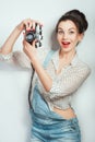 Fashion look, surprised young woman model with retro film camera wearing in denim clothes posing on white wall. Expressive beauty