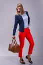 Fashion look of woman dressed red pants, blue jacket, brown bag. model looks at a leather bag. full height Royalty Free Stock Photo