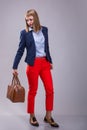 Fashion look of woman dressed red pants, blue jacket, brown bag. model looks at a leather bag. full height Royalty Free Stock Photo