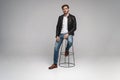 Fashion man, Handsome serious beauty male model portrait wear leather jacket, sitting on chair over white background. Royalty Free Stock Photo