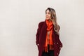 Fashion model attractive young woman in elegant stylish burgundy coat with orange bright fashionable scarf stands near vintage Royalty Free Stock Photo