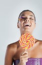 Fashion model with bird feather eyelashes smiles and holds a rainbow lollipop Royalty Free Stock Photo