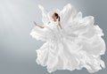 Fashion Model in Creative Pure White Dress as Cloud. Woman in Long Silk Gown with Chiffon Fabric flying on Wind over Light Gray Royalty Free Stock Photo