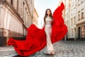 Fashion Model in Evening Dress with Flying Red Fabric. Woman Walking in City. Outdoor Urban Glamour Full Length Portrait Royalty Free Stock Photo