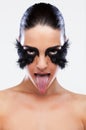 Fashion model with false feather colourful eyelashes bold eye makeup tongue out Royalty Free Stock Photo