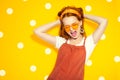 Fashion model girl over yellow polka dots background. Beauty stylish redhead woman posing in urban clothes and yellow sunglasses Royalty Free Stock Photo