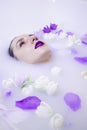 Fashion model girl with violet make-up in milk bath with violet flowers