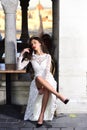 Fashion model with glamour look and makeup. Sexy woman sit alone in street cafe. Woman in white wedding dress outdoor