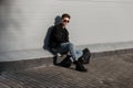 Fashion model handsome young man with trendy hairstyle in sunglasses in black denim jacket in blue jeans in sneakers with backpack Royalty Free Stock Photo