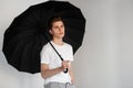 Fashion model handsome young man in youth fashionable T-shirt stands with vintage umbrella near wall in room. Sexy modern nice guy