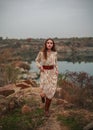 Fashion model in long dress and brown boots poses by the lake in countryside