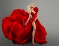 Fashion Model in Red Long Dress waving on Wind. Glamour Girl dancing showing Sexy Leg. Stylish Blond Woman in Evening Silk Gown Royalty Free Stock Photo