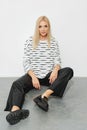 Fashion model in a striped sweater and wide leather pants sits on the floor