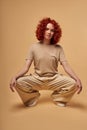 Fashion model with stylish wavy red hair posing at camera in beige casual outfit