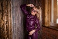 Fashion model in sunglasses, purple leather jacket, leather pants posing with hand in pocket near wooden wall. Spring style,
