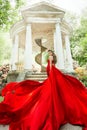 Fashion Model Waving Long Fluttering Red Dress, Woman in Garden, Old White Alcove in Flowers Royalty Free Stock Photo