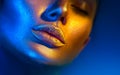 Fashion model woman face in bright sparkles, colorful neon lights, beautiful sexy girl lips. Trendy glowing gold skin makeup Royalty Free Stock Photo