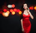 Fashion model woman in red silky dress and black carnival mask on background with abstract night glitter bokeh Royalty Free Stock Photo