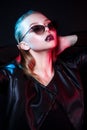 Fashion model woman in sunglasses in colorful bright neon lights posing in studio