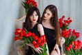 Fashion models in tender black dresses posing in sensual way at luxury interior full of tulips. Young woman sensuality.