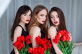 Fashion models in tender black dresses posing in sensual way at luxury interior full of tulips. Young woman sensuality.