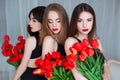 Fashion models in tender black dresses posing in sensual way at luxury interior full of tulips. Young woman sensuality.