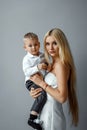 Fashion mom in a white elegant outfit and a baby on a gray background. Feminism concept, mother`s day