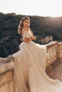 Beautiful bride with blond hair in luxurious wedding dress posing in balcony with beautiful view of mountains and sea