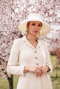 Sensual woman with blond hair in elegant dress and accessories posing among blossoming peach trees in park Royalty Free Stock Photo