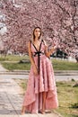 Sensual woman with blond hair in elegant dress and accessories posing among blossoming peach trees in park Royalty Free Stock Photo