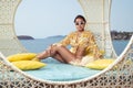 Fashion outdoor photo of beautiful girl posing on the wicker nest chair Royalty Free Stock Photo