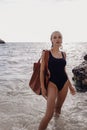 Beautiful sexy woman with dark hair in elegant swimming suit posing on the summer sunset beach Royalty Free Stock Photo