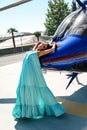 Beautiful sexy woman with dark hair in luxurious dress posing near blue helicopter