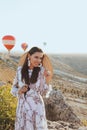 Beautiful woman with dark hair in elegant dress having picnic with fantastic view on valley with air balloons on background