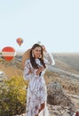 Beautiful woman with dark hair in elegant dress having picnic with fantastic view on valley with air balloons on background