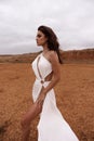 beautiful woman with dark hair in luxurious white dress with accessories posing in desert in Cyprus