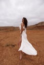 beautiful woman with dark hair in luxurious white dress with accessories posing in desert in Cyprus