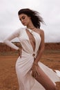 beautiful woman with dark hair in luxurious white dress with accessories posing in desert in Cyprus