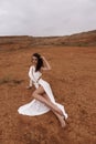 beautiful woman with dark hair in luxurious white dress with accessories posing in desert in Cyprus