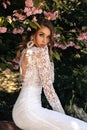 Beautiful women in luxurious wedding dresses with accessories posing in garden with blossoming sakura trees