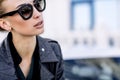 Fashion outdoor photo of beautiful woman with dark hair in black leather jacket and sunglasses posing in luxurious auto Royalty Free Stock Photo