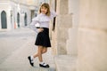 Fashion outdoor portrait of charming little girl in white blouse and black skirt, posing leaning on the wall of Royalty Free Stock Photo