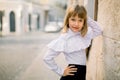 Fashion outdoor portrait of charming little girl in white blouse and black skirt, posing leaning on the wall of Royalty Free Stock Photo