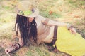 Fashion outdoor woman portrait with dreadlocks, dressed in knitted top, yellow skirt and straw hat, resting on the dry grass in pa Royalty Free Stock Photo