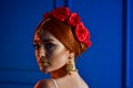 Fashion photo of beautiful girl under white veil and red flowers on her head on blue background Royalty Free Stock Photo