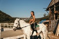 Beautiful woman with dark hair in elegant sportive suit posing near white horse in stable Royalty Free Stock Photo